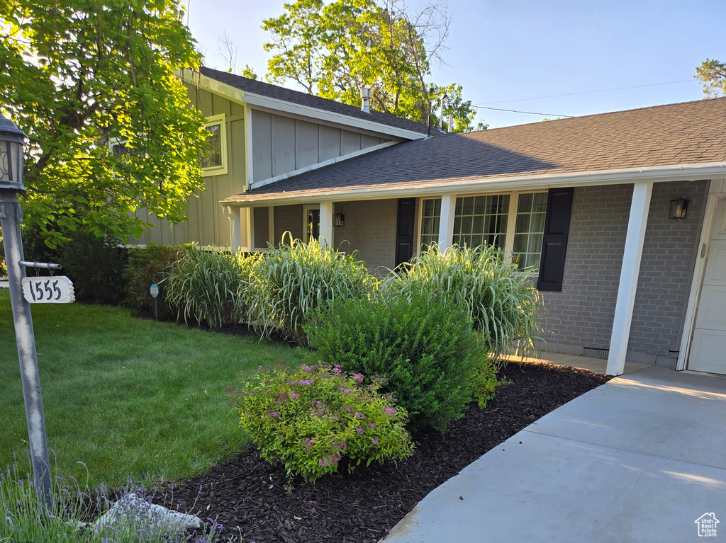 View of property exterior with brick siding, an attached garage, a lawn, concrete driveway, and board and batten siding