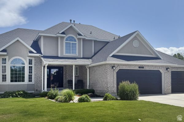 Traditional-style house with a front lawn, concrete driveway, an attached garage, stucco siding, and brick siding