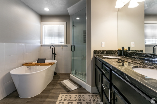 Bathroom featuring double vanity, a freestanding tub, wood finished floors, a shower stall, and tile walls