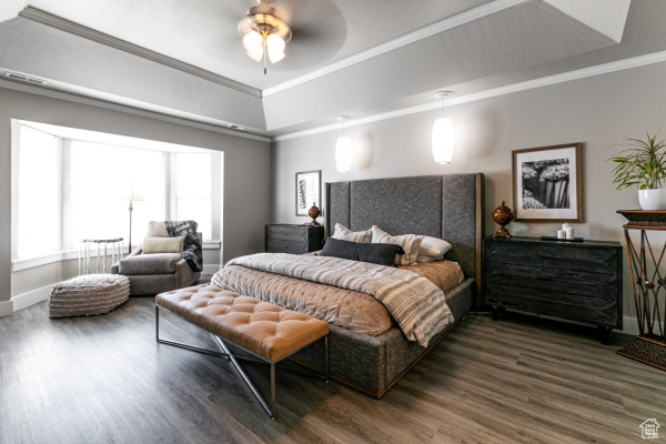 Bedroom with dark wood-style floors, baseboards, crown molding, a tray ceiling, and a ceiling fan