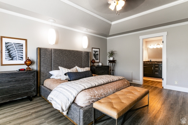Bedroom with wood finished floors, a tray ceiling, ornamental molding, baseboards, and connected bathroom