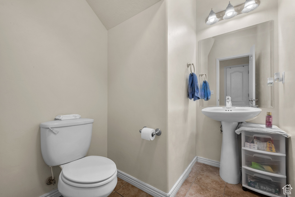 Half bathroom featuring toilet, vaulted ceiling, baseboards, tile patterned floors, and a sink