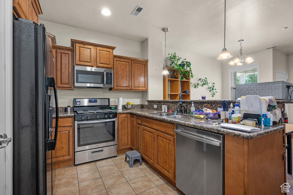 Kitchen featuring stainless steel appliances, brown cabinets, a peninsula, light tile patterned floors, and pendant lighting