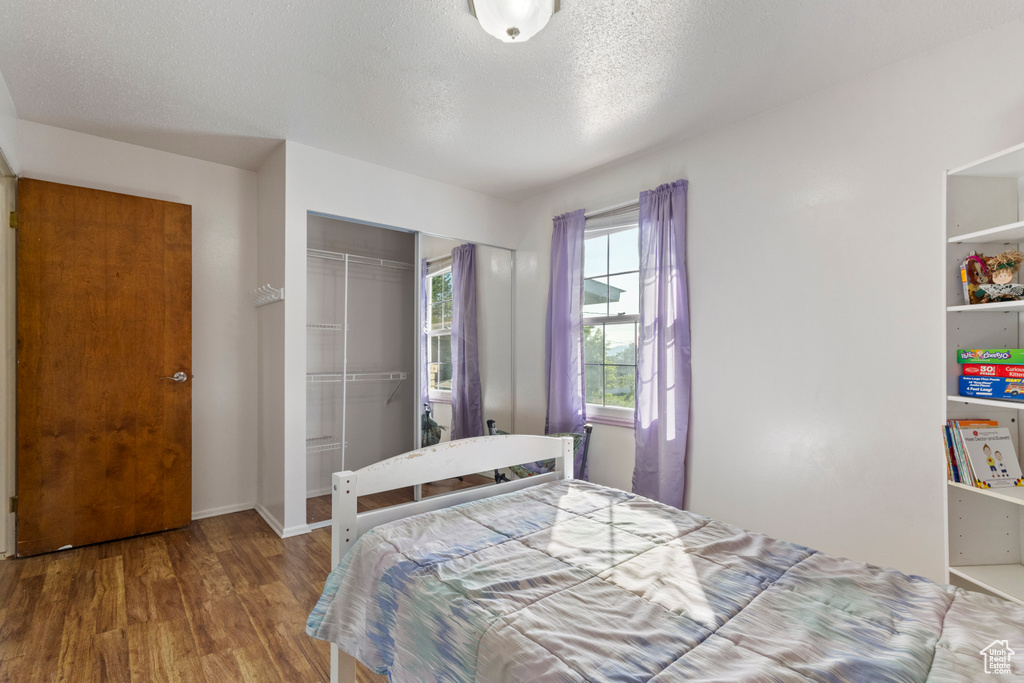 Bedroom featuring wood finished floors, a closet, a textured ceiling, and baseboards