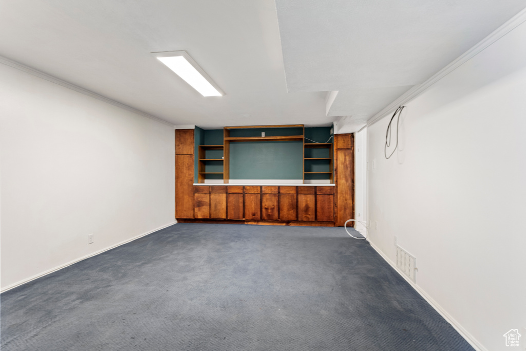 Finished basement with dark colored carpet, baseboards, and ornamental molding