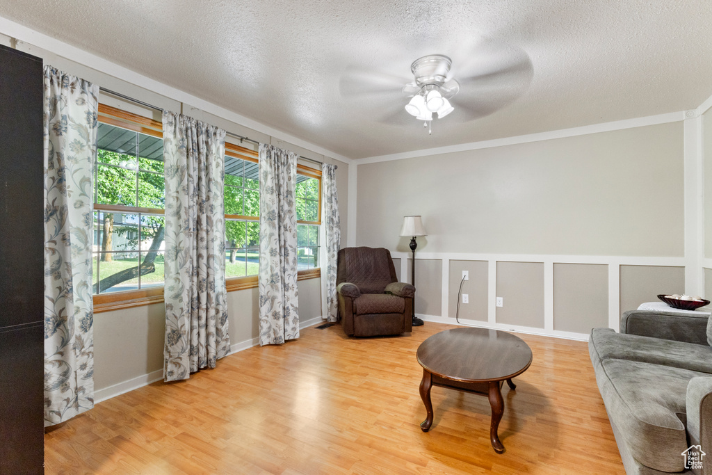 Living area with wood finished floors, a ceiling fan, a textured ceiling, crown molding, and baseboards