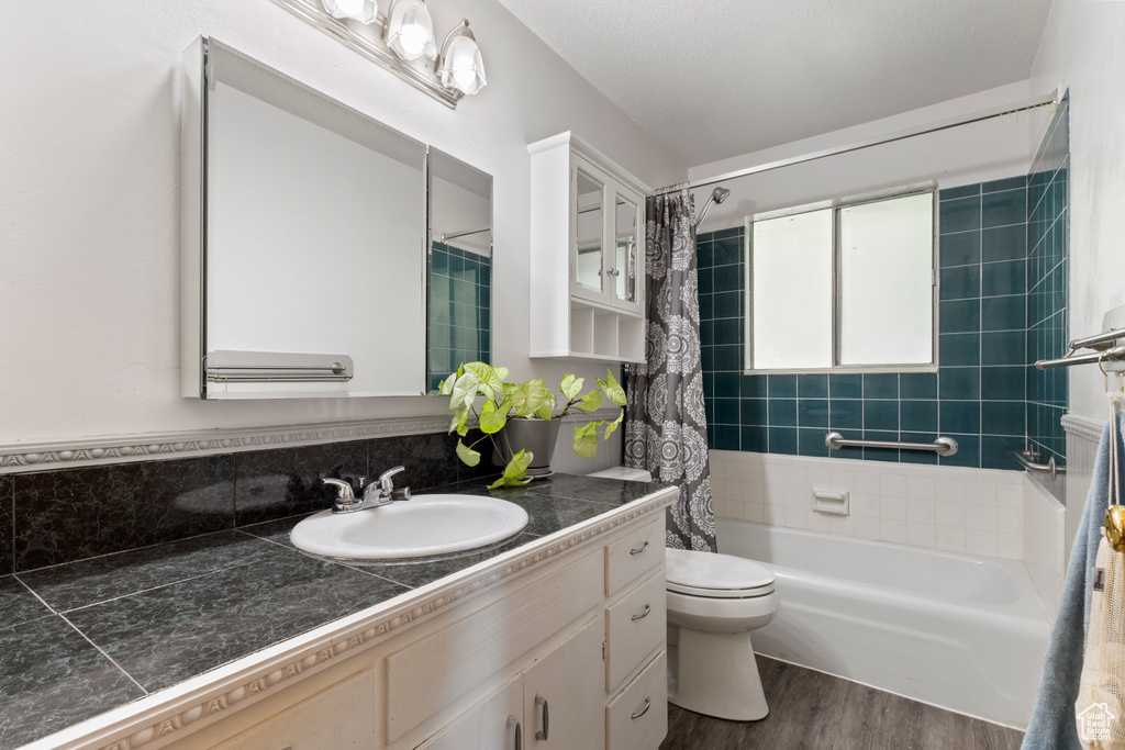 Bathroom featuring vanity, wood finished floors, shower / bathtub combination with curtain, and toilet