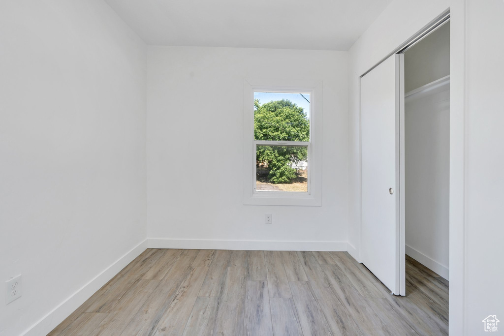 Unfurnished bedroom featuring light wood-style flooring, a closet, and baseboards