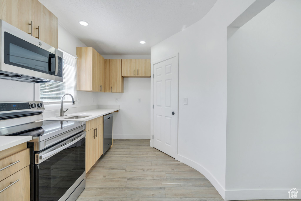 Kitchen featuring stainless steel appliances, light brown cabinetry, a sink, light wood finished floors, and light countertops