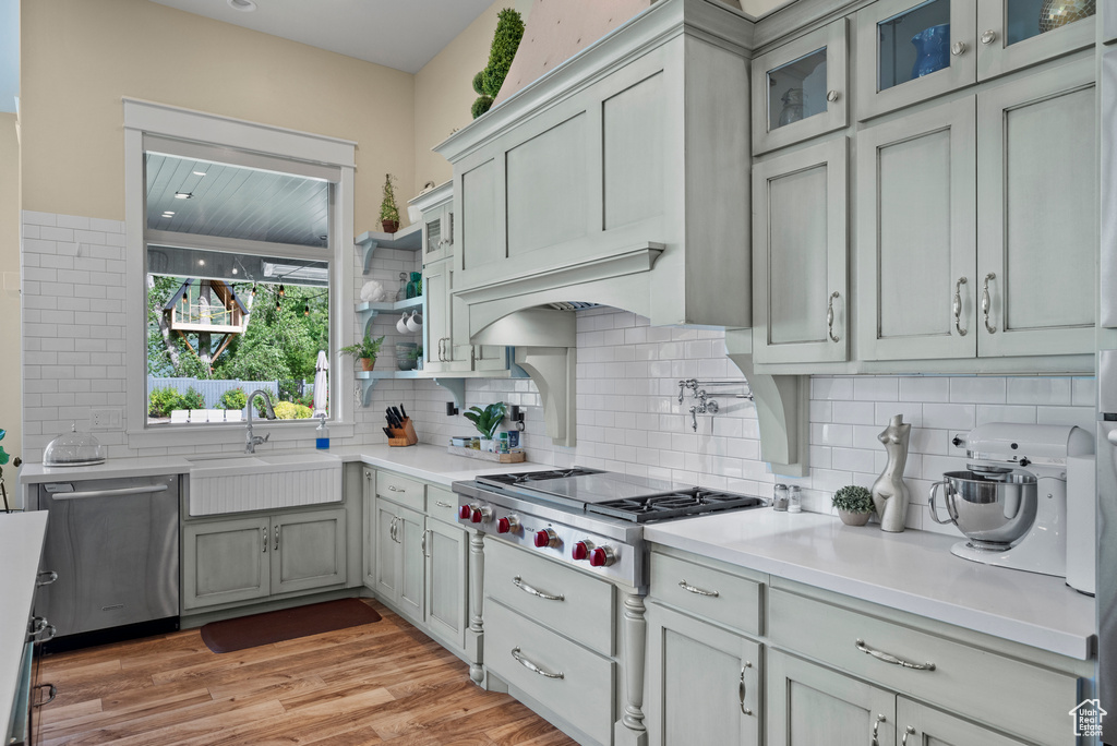 Kitchen with a sink, stainless steel appliances, backsplash, light countertops, and light wood-style floors