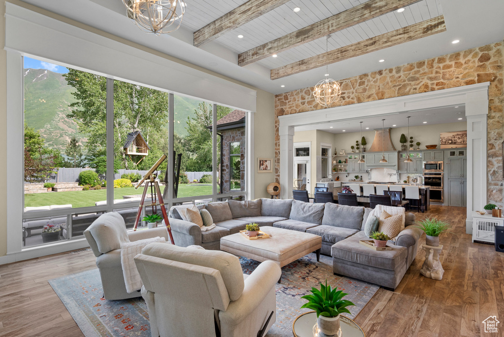 Living room featuring a chandelier, healthy amount of natural light, wood ceiling with exposed beams, a high ceiling, and light wood-style floors
