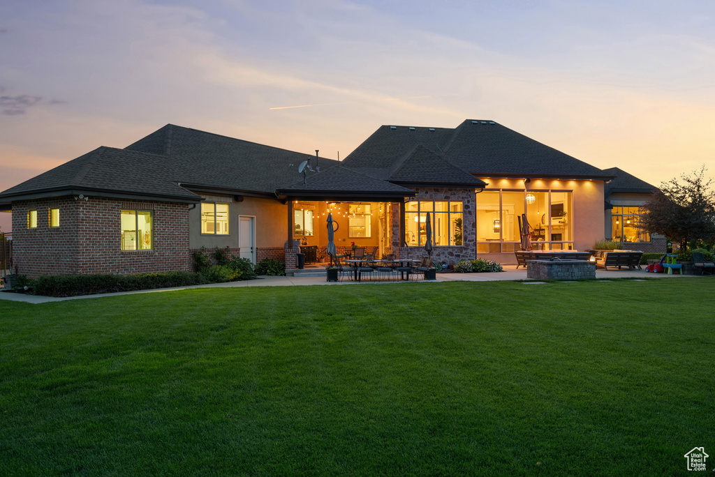 Rear view of property featuring a fire pit, a patio, a yard, brick siding, and roof with shingles