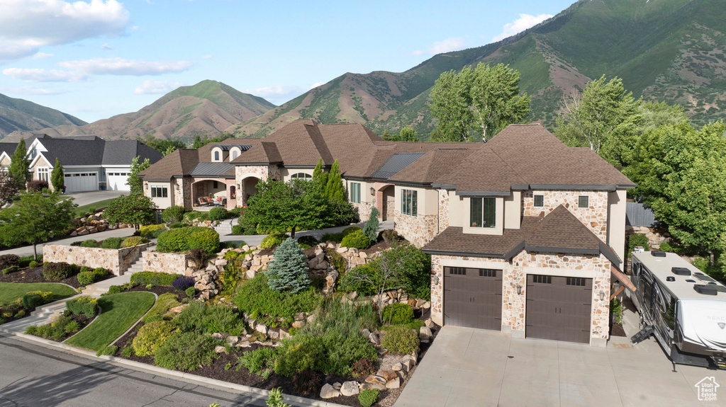 View of front of home with stone siding, concrete driveway, an attached garage, and a mountain view