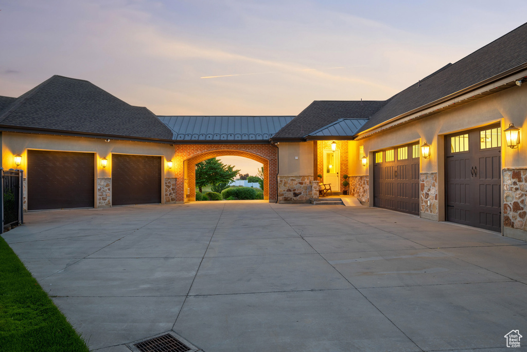 View of front of property featuring a garage, a standing seam roof, driveway, stone siding, and metal roof