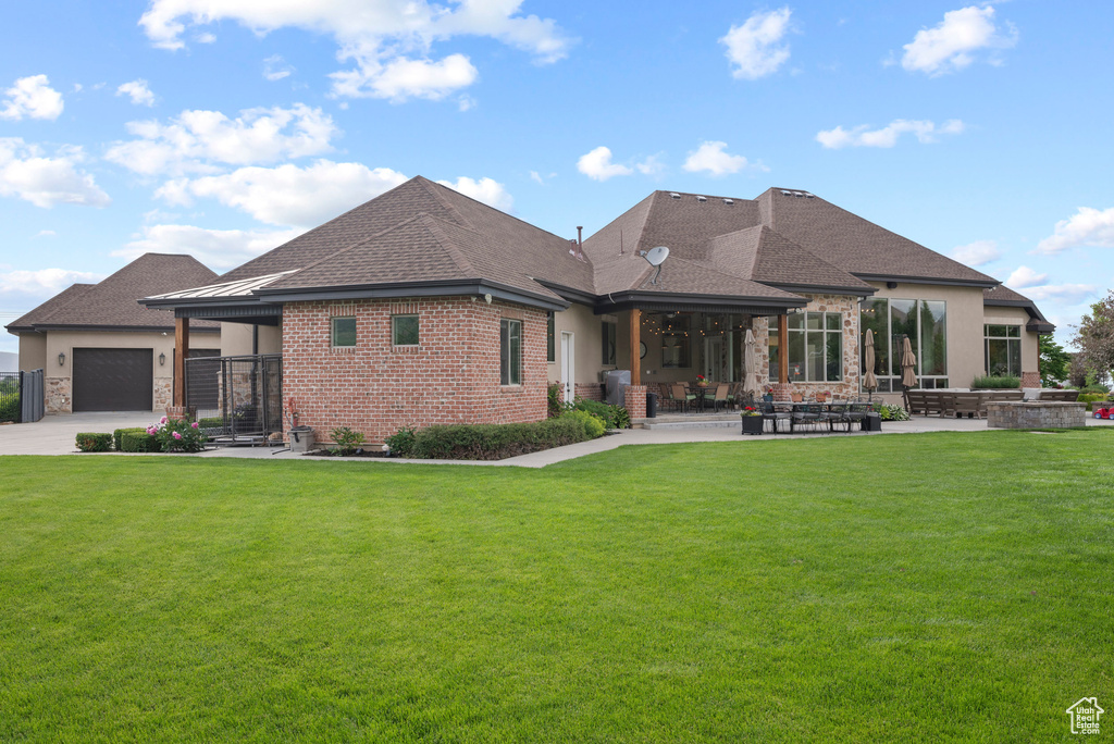 Rear view of house featuring a yard, a patio area, roof with shingles, and a garage
