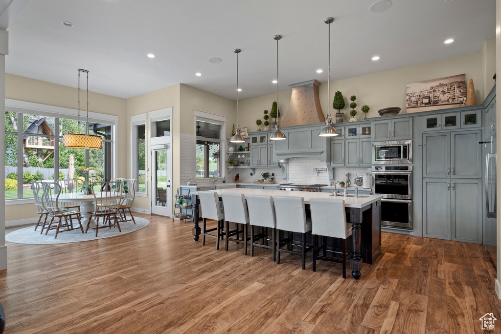 Kitchen with appliances with stainless steel finishes, light countertops, wood finished floors, tasteful backsplash, and recessed lighting