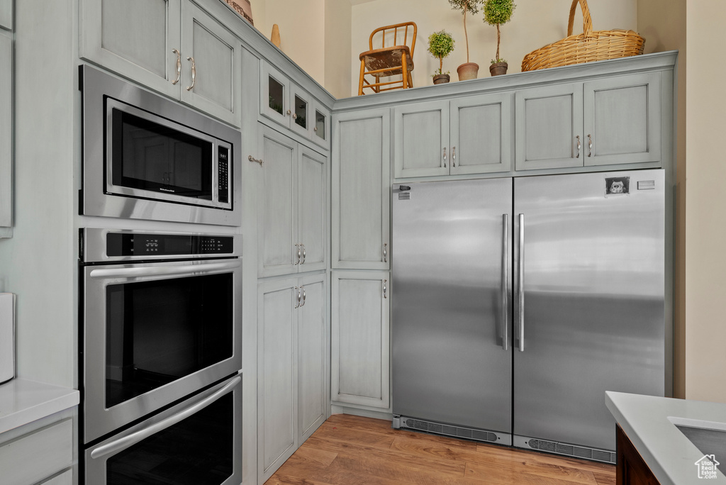 Kitchen featuring built in appliances, light countertops, glass insert cabinets, and light wood finished floors