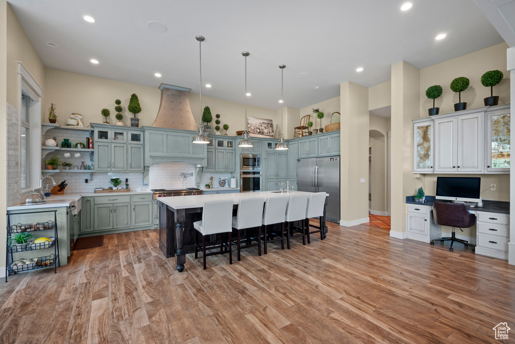 Kitchen featuring stainless steel appliances, a breakfast bar, decorative backsplash, open shelves, and light wood-type flooring