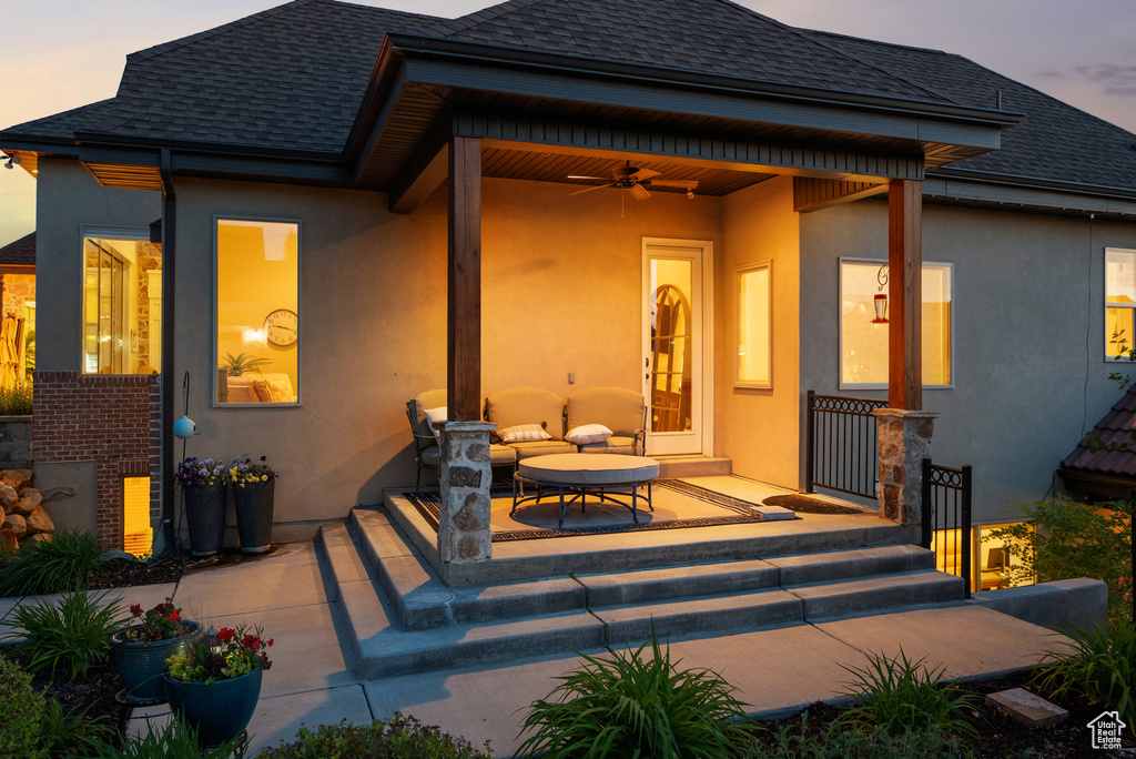 Back of property at dusk with roof with shingles, stucco siding, and ceiling fan