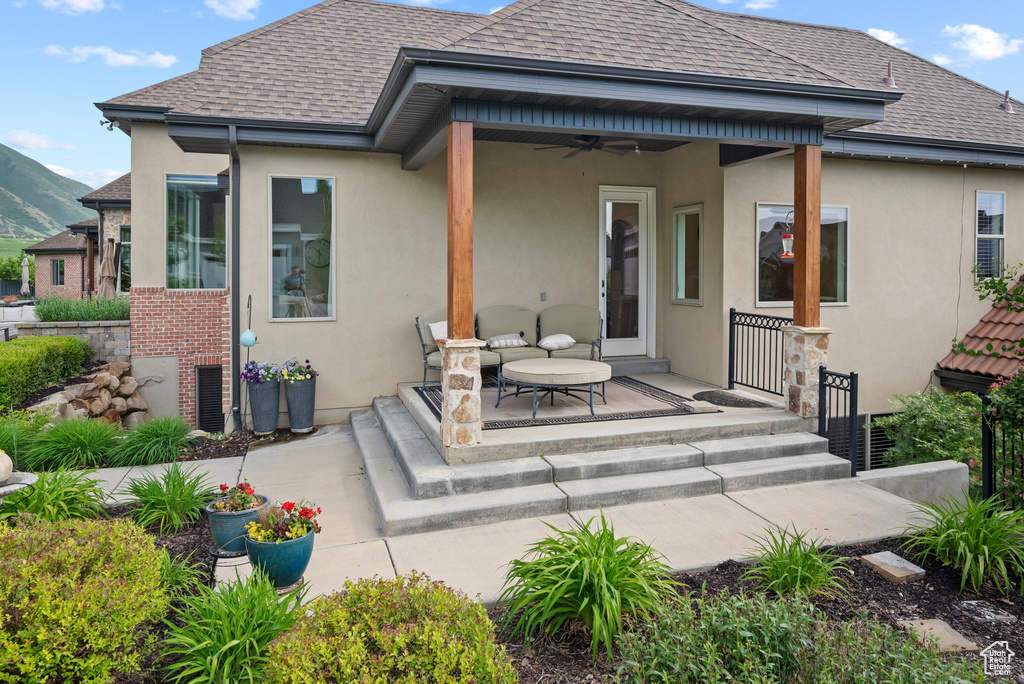 Back of property with a ceiling fan, stucco siding, a shingled roof, and a mountain view
