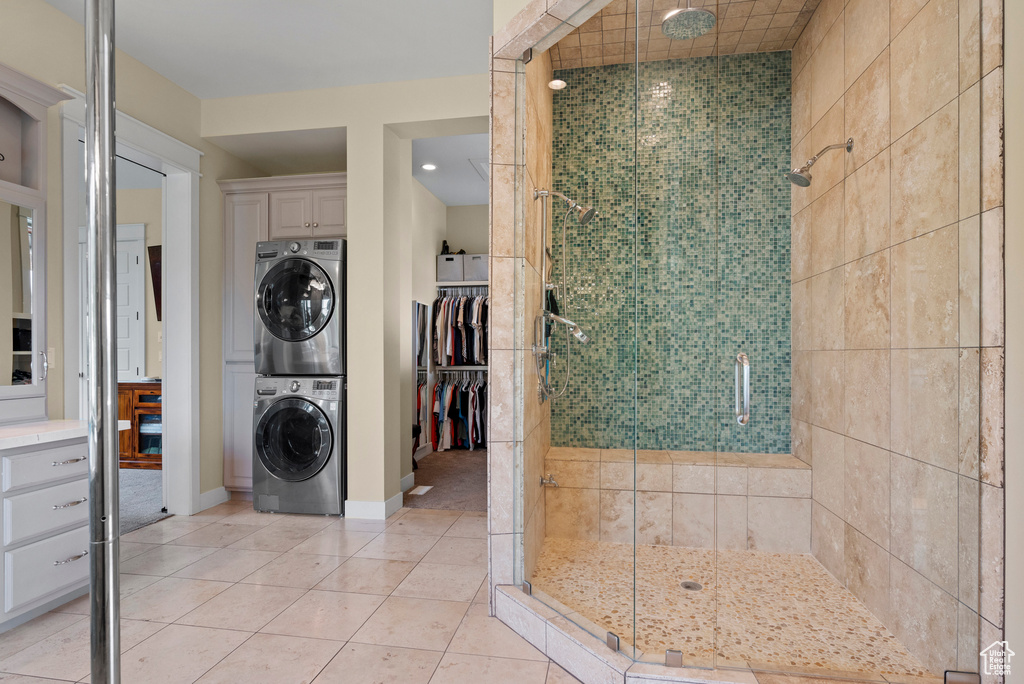 Bathroom featuring stacked washer and clothes dryer, a shower stall, tile patterned floors, baseboards, and a spacious closet