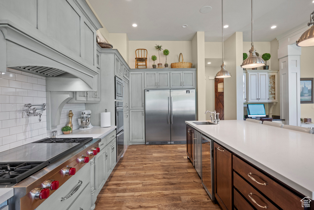 Kitchen with built in appliances, custom exhaust hood, a sink, light wood-type flooring, and light countertops