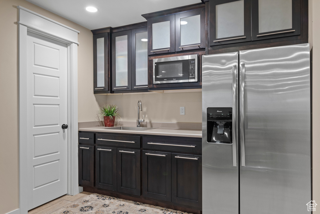 Kitchen featuring appliances with stainless steel finishes, a sink, light countertops, glass insert cabinets, and recessed lighting
