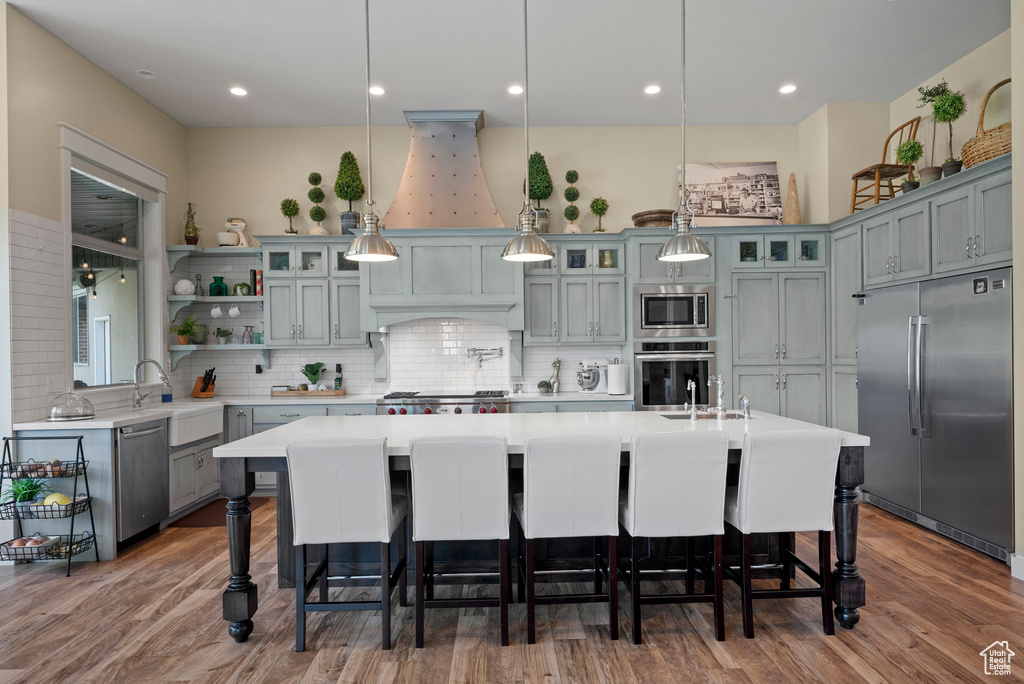 Kitchen featuring built in appliances, light countertops, backsplash, wood finished floors, and recessed lighting