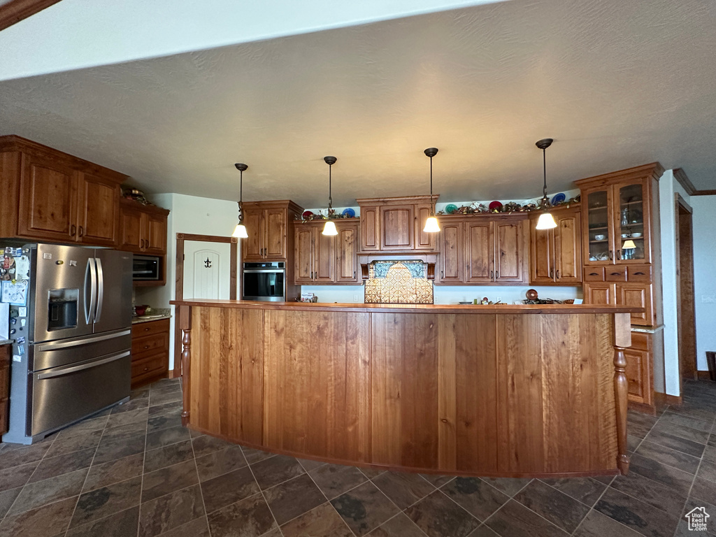 Kitchen with stainless steel appliances, brown cabinets, glass insert cabinets, and dark stone finish floors