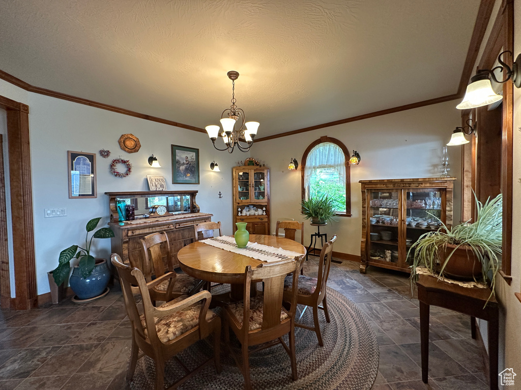 Dining room with a chandelier, ornamental molding, baseboards, and dark stone finish flooring