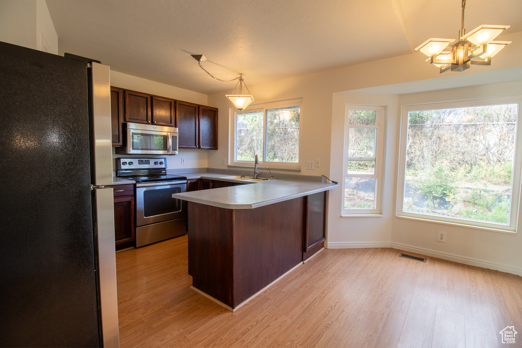 Kitchen featuring stainless steel appliances, a peninsula, light wood-style flooring, and a chandelier