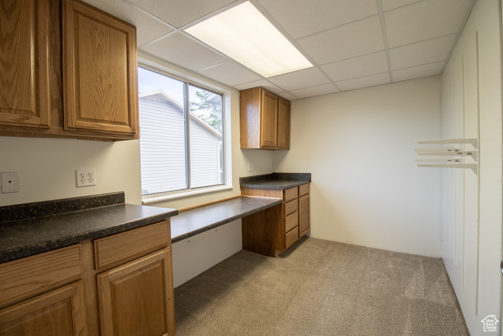 Kitchen with dark countertops, light carpet, brown cabinetry, and a drop ceiling