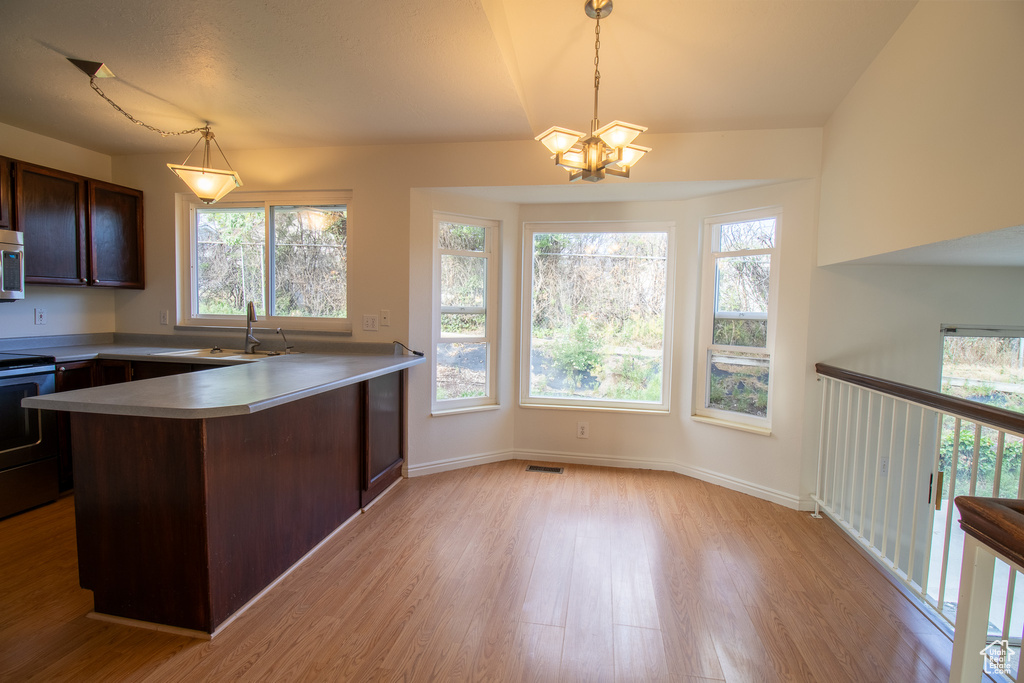 Kitchen featuring a sink, stainless steel range with electric stovetop, a peninsula, light wood-style floors, and a chandelier