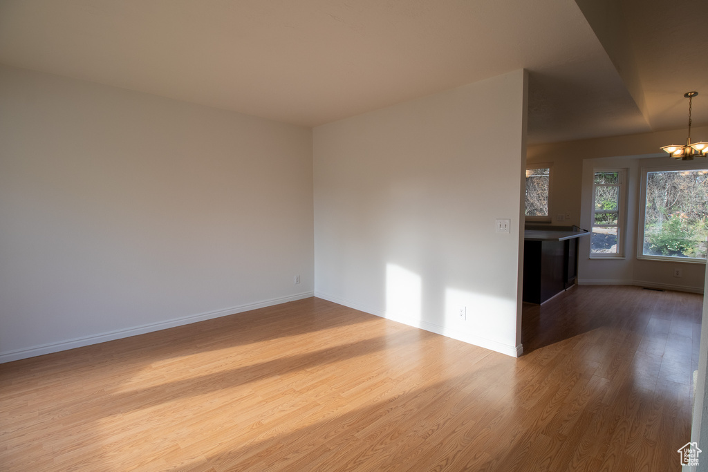 Unfurnished living room featuring dark wood-type flooring, a chandelier, and baseboards