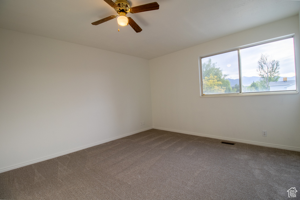 Carpeted spare room featuring ceiling fan and baseboards