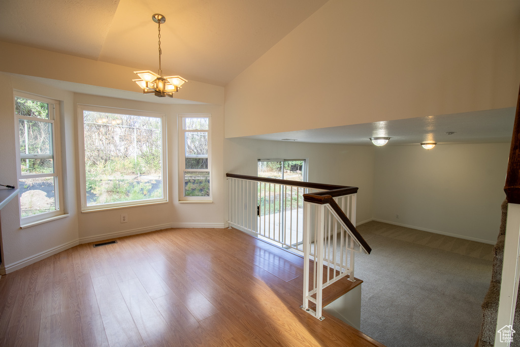 Unfurnished room with a chandelier, plenty of natural light, vaulted ceiling, and baseboards