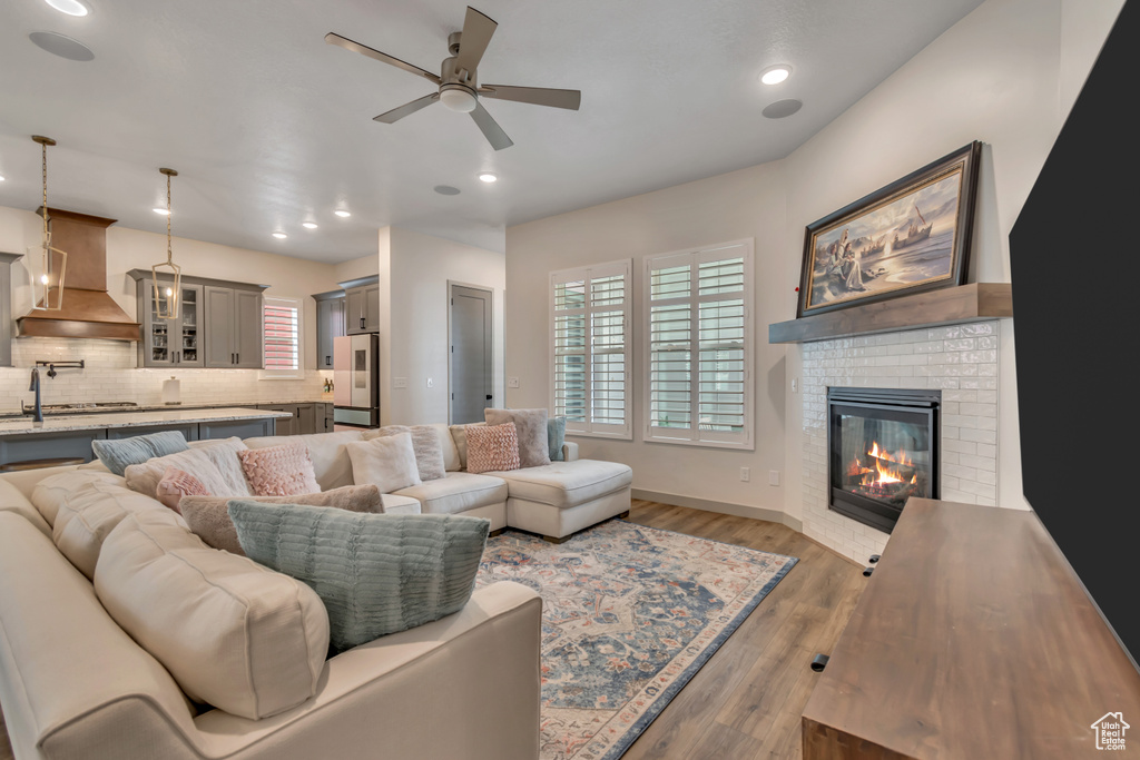 Living room with ceiling fan, a fireplace, light wood-style flooring, and recessed lighting