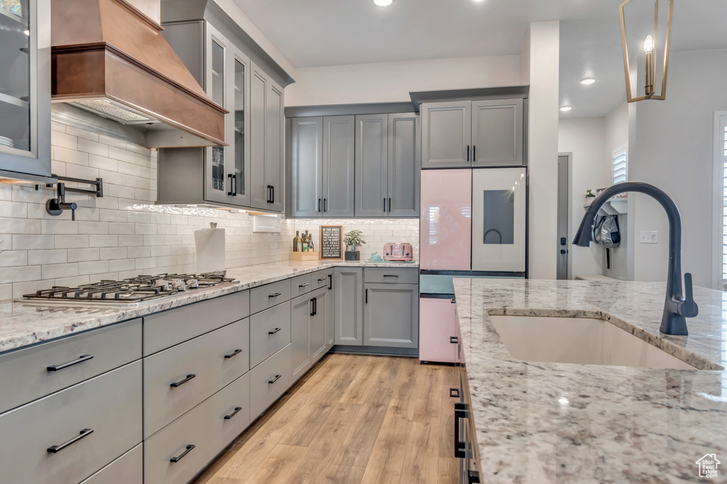 Kitchen featuring stainless steel gas stovetop, gray cabinetry, custom exhaust hood, light wood-type flooring, and light stone countertops