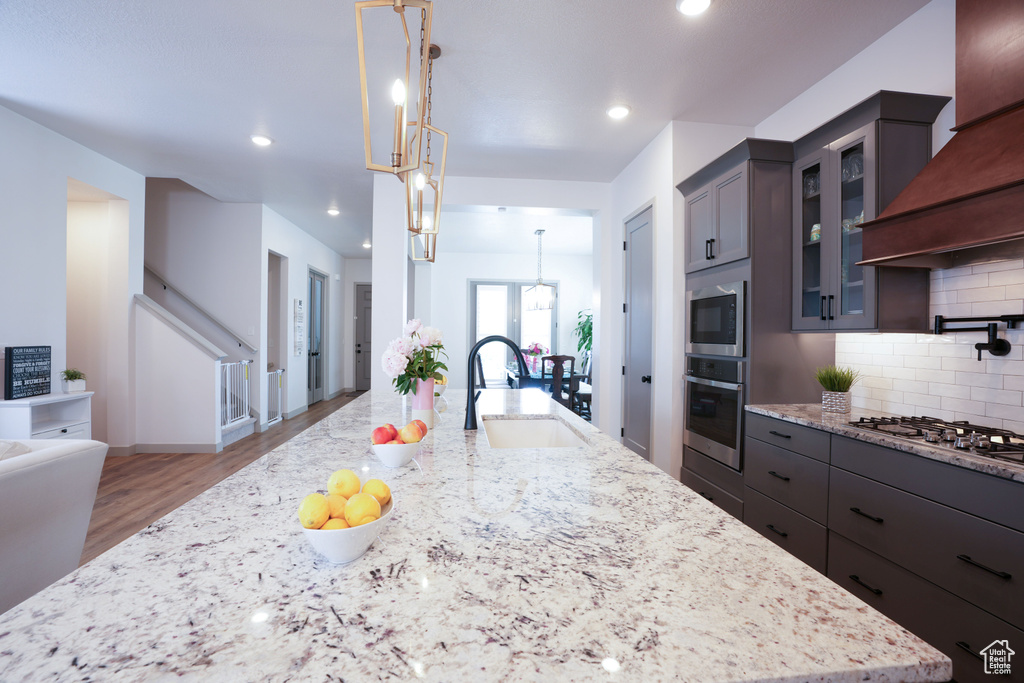 Kitchen with appliances with stainless steel finishes, a sink, decorative backsplash, light wood-type flooring, and light stone countertops
