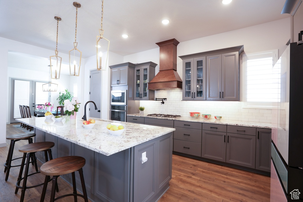 Kitchen with stainless steel appliances, custom exhaust hood, a sink, gray cabinets, and recessed lighting