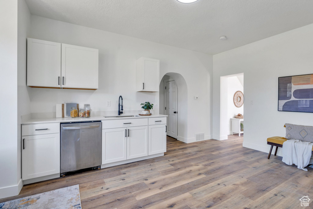 Kitchen with stainless steel dishwasher, a sink, light wood finished floors, and white cabinetry