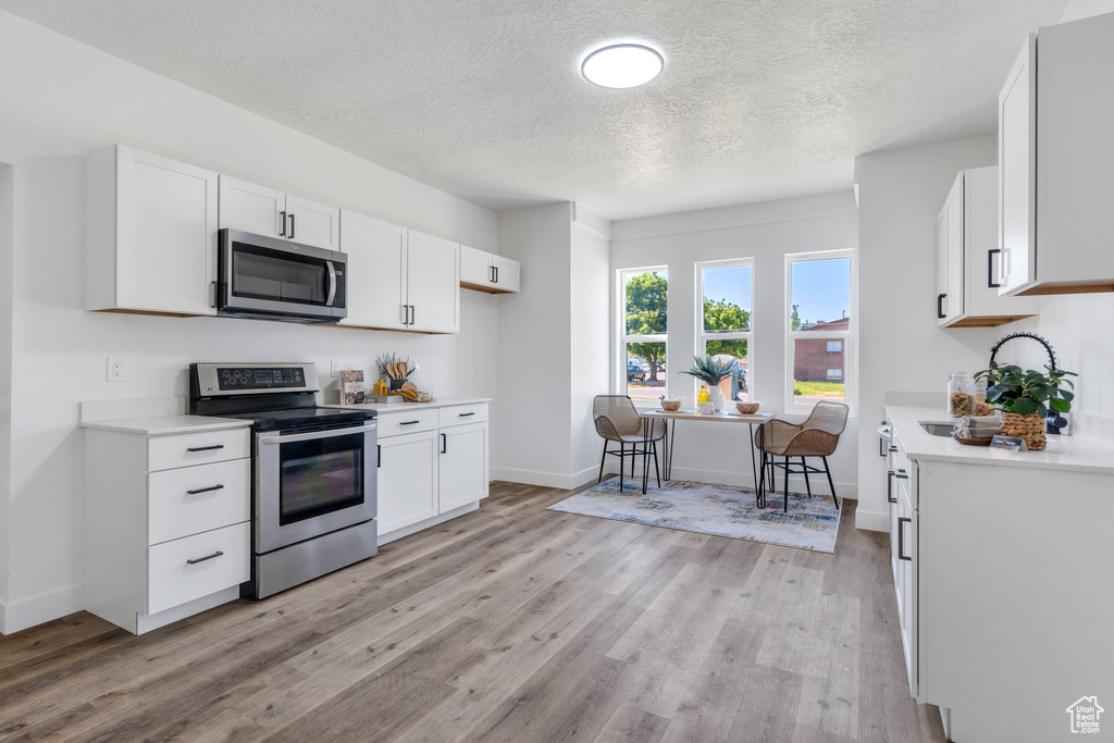 Kitchen with appliances with stainless steel finishes, light countertops, light wood-type flooring, a textured ceiling, and white cabinets