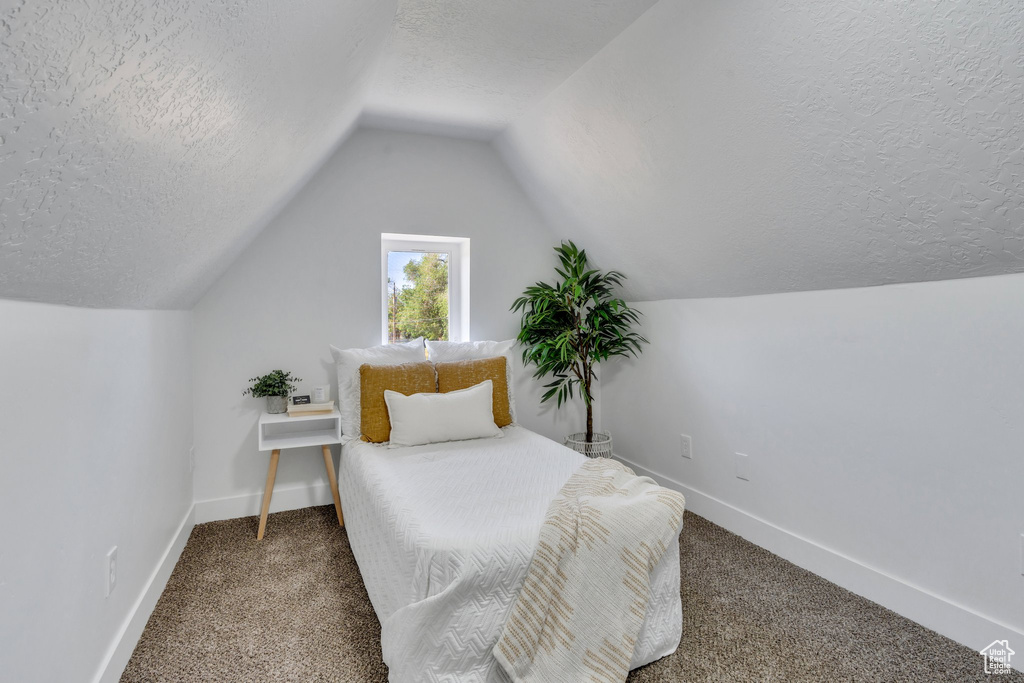 Carpeted bedroom with a textured ceiling, baseboards, and vaulted ceiling