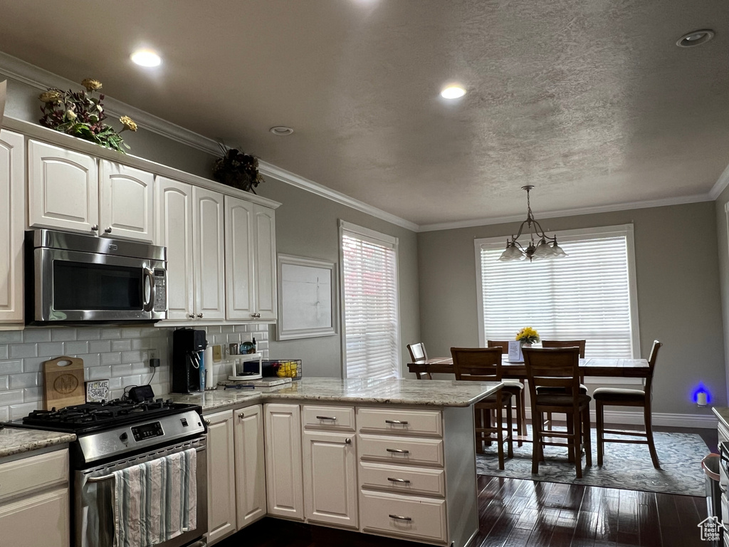Kitchen with stainless steel appliances, dark wood finished floors, a peninsula, decorative backsplash, and white cabinets