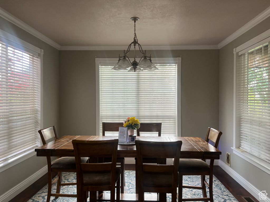Dining space featuring a chandelier, dark wood-type flooring, plenty of natural light, baseboards, and crown molding