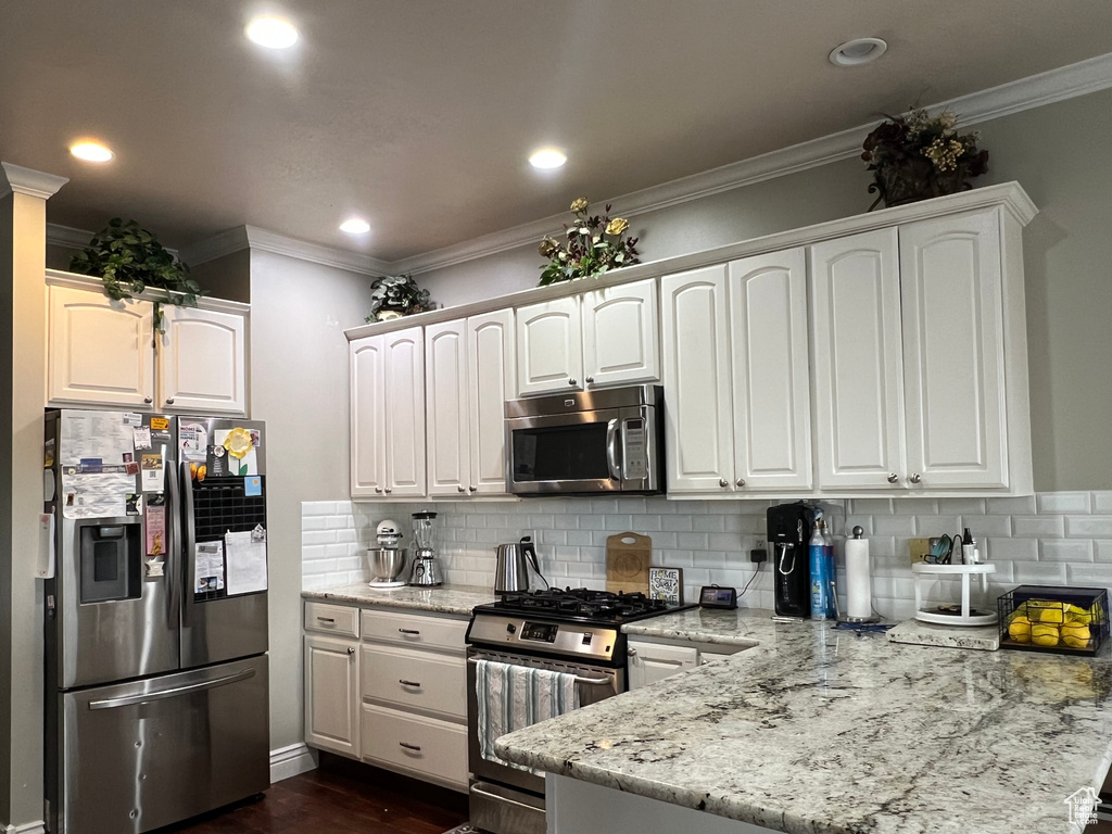 Kitchen featuring stainless steel appliances, a peninsula, crown molding, tasteful backsplash, and white cabinetry