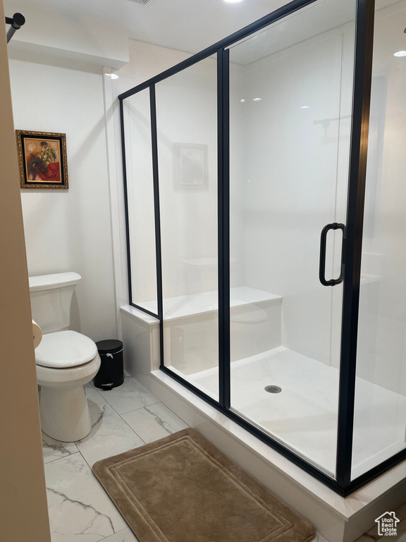 Bathroom with marble finish floors, toilet, and a stall shower
