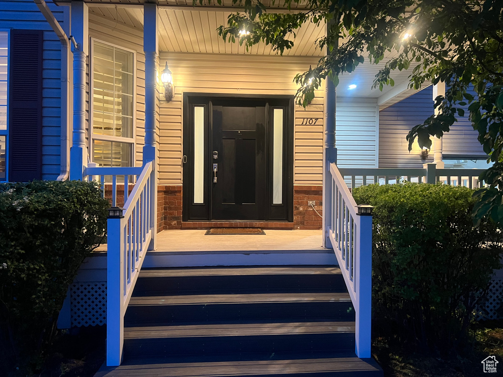 View of exterior entry featuring covered porch and brick siding