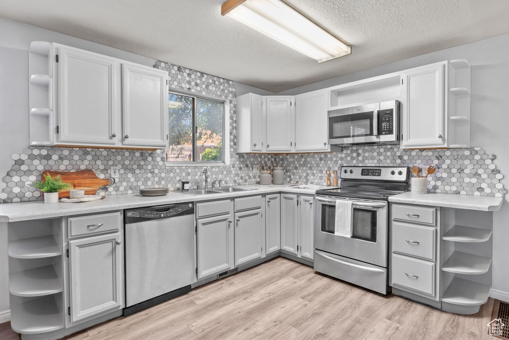 Kitchen featuring open shelves, appliances with stainless steel finishes, and a textured ceiling