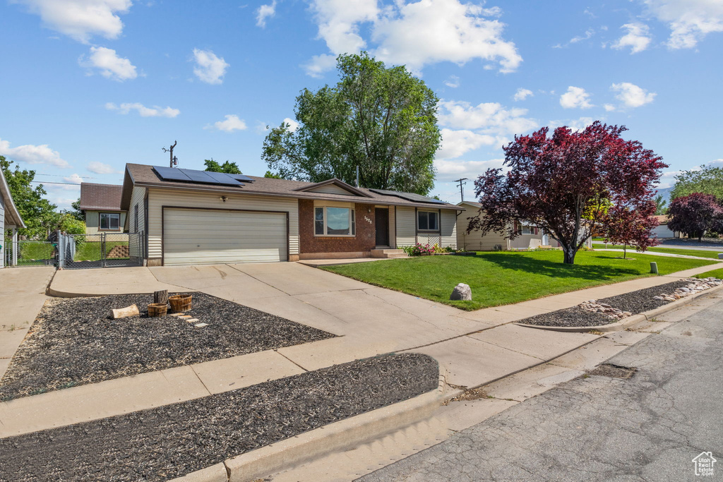 Ranch-style home featuring an attached garage, concrete driveway, roof mounted solar panels, brick siding, and a gate